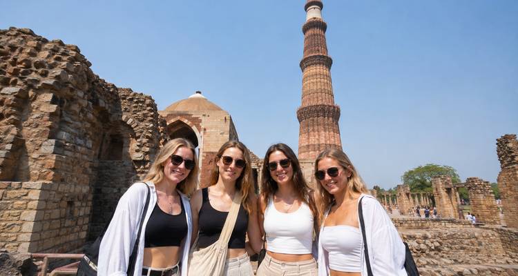 Quatre jeunes femmes posant ensemble à la base du Qutub Minar au milieu des ruines de pierre historiques.