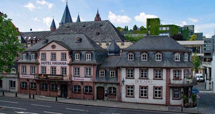 Complejo histórico de posada y restaurante con techo de pizarra en Mainz con torres de iglesia elevándose detrás.