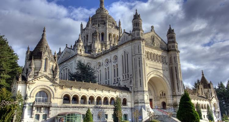 Grande Basilique néo-byzantine Sainte-Thérèse avec ses tours ornées et ses escaliers majestueux sous des nuages dramatiques.