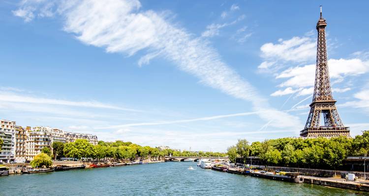 La Tour Eiffel emblématique s'élevant aux côtés de la Seine avec des ciels bleus striés de traînées de condensation et des berges vertes.