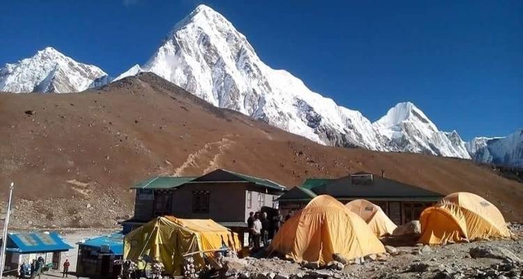 Zelte vor einem schneebedeckten Gebirgszug unter klarem Himmel.