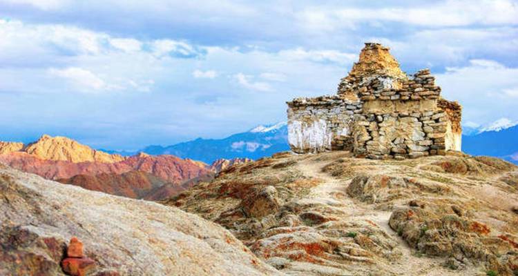 Ancienne structure de pierre sur une colline rocheuse avec des montagnes en arrière-plan.