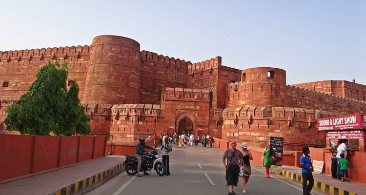 Besucher, die zu Fuß gehen und Motorräder fahren, vor den massiven Mauern aus rotem Sandstein des Agra Fort