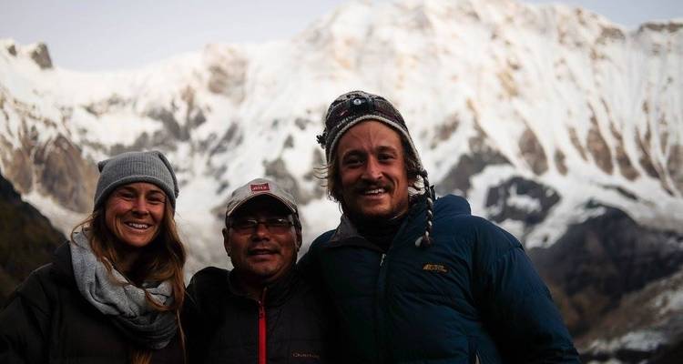 Three people posing in front of snowy mountains.