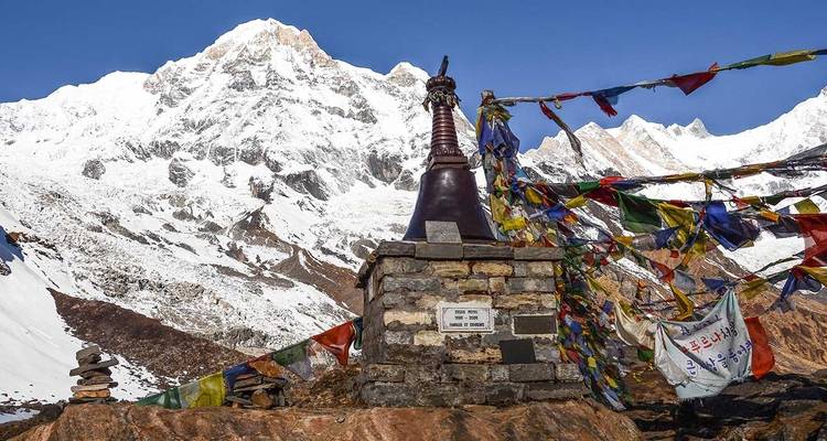 Stupa with prayer flags and snow-covered mountains in the background.