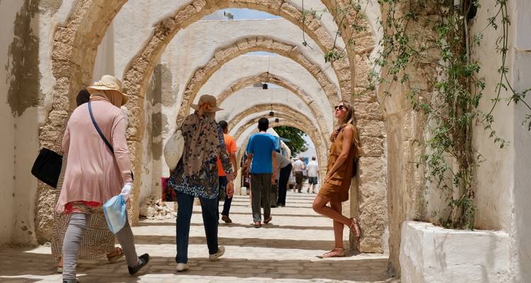 Des personnes marchant sous des arches de pierre dans un cadre historique.