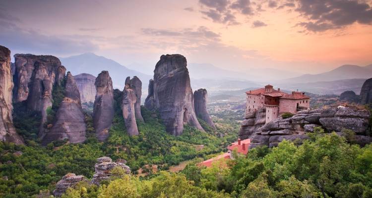 Sunset over a valley with rock formations and a monastery.