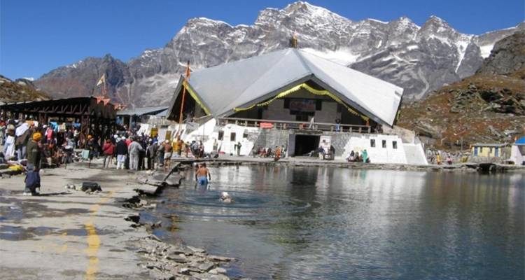 Pilgrims bathing in a lake beside a worship site with mountains behind.