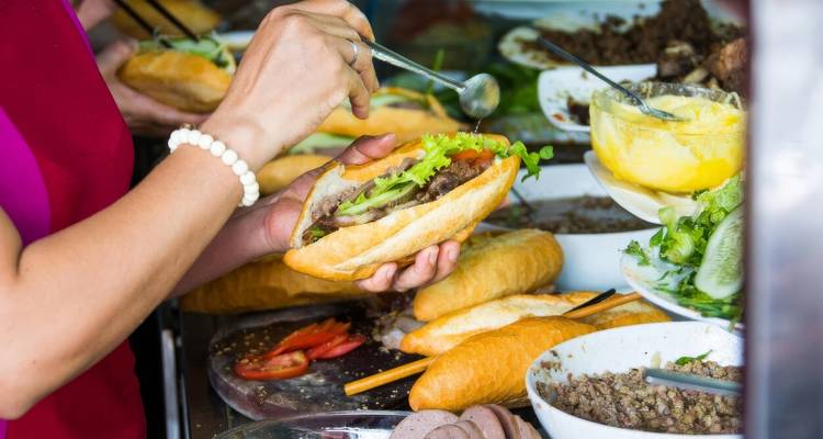 Persoon die een Vietnamese baguette bereidt met verschillende ingrediënten.