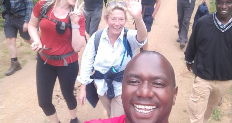 A group of people smiling and waving while hiking on a dirt path.
