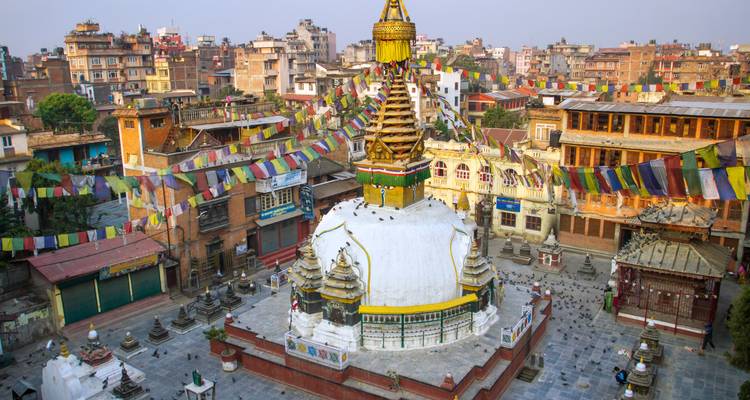 Stupa with prayer flags in a city surrounded by buildings.