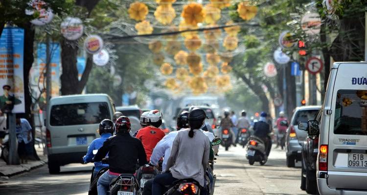 Calle concurrida de una ciudad vietnamita llena de motocicletas bajo decoraciones amarillas festivas.