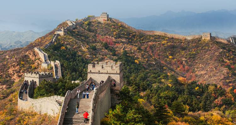 Section spectaculaire de la Grande Muraille de Chine serpentant sur des montagnes aux couleurs automnales avec des touristes marchant sur les remparts.