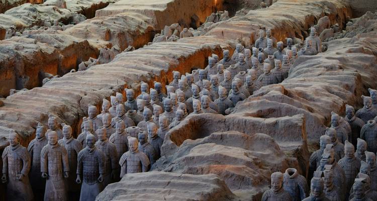 Rangées de Guerriers en Terre Cuite se dressant dans des fosses excavées sous un éclairage intérieur doux à Xi'an.
