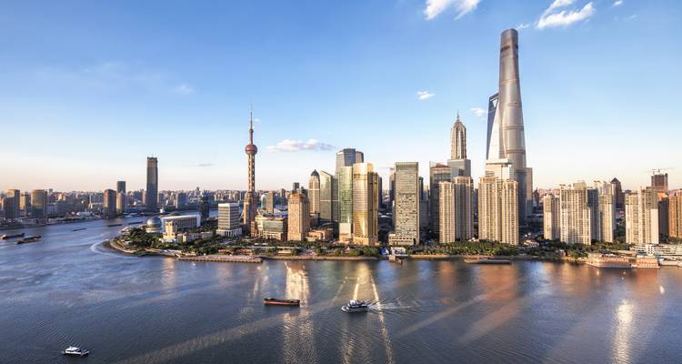 Panorama aérien du quartier financier de Shanghai le long du fleuve Huangpu à la lumière de fin d'après-midi avec des bateaux sur l'eau.