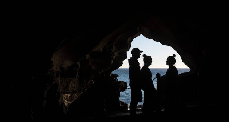 Silhouettes of tourists exploring a cave with sea view.