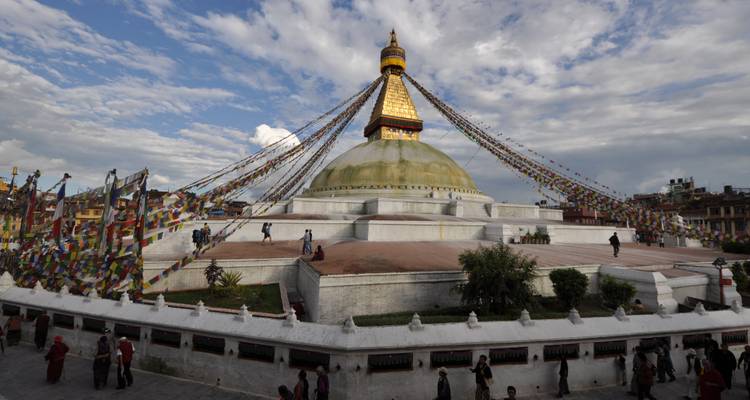 A large stupa surrounded by prayer flags and people.