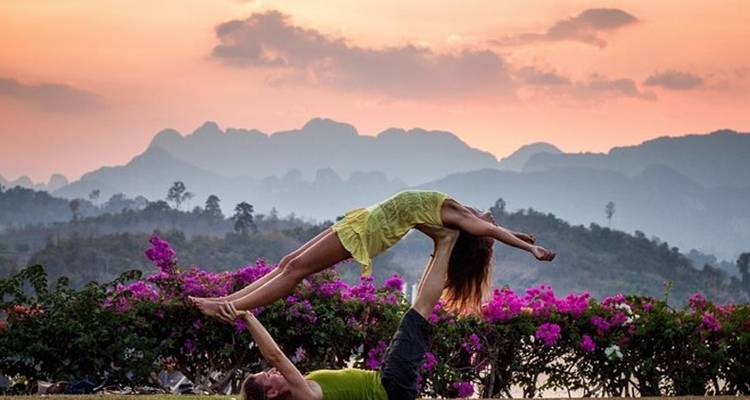Couple pratiquant l'acro yoga pendant un coucher de soleil coloré.
