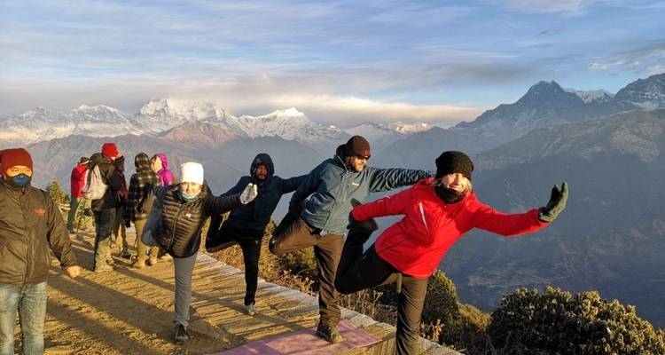 Groupe pratiquant le yoga sur un sentier de montagne avec des sommets enneigés.