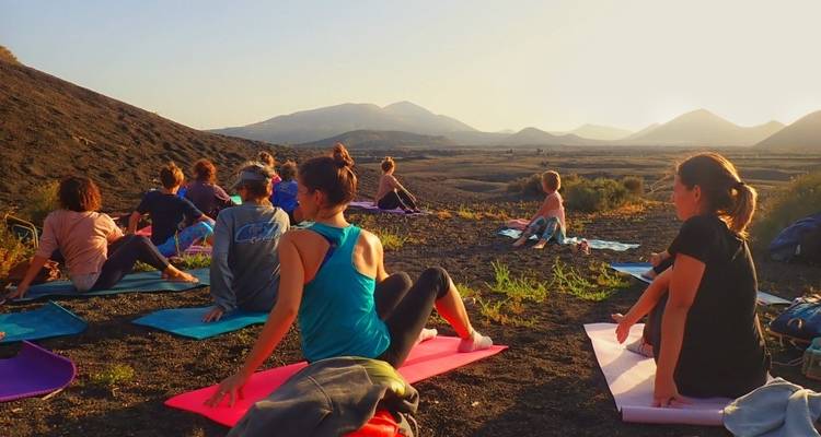 Cours de yoga assis sur des tapis avec vue sur une région montagneuse.