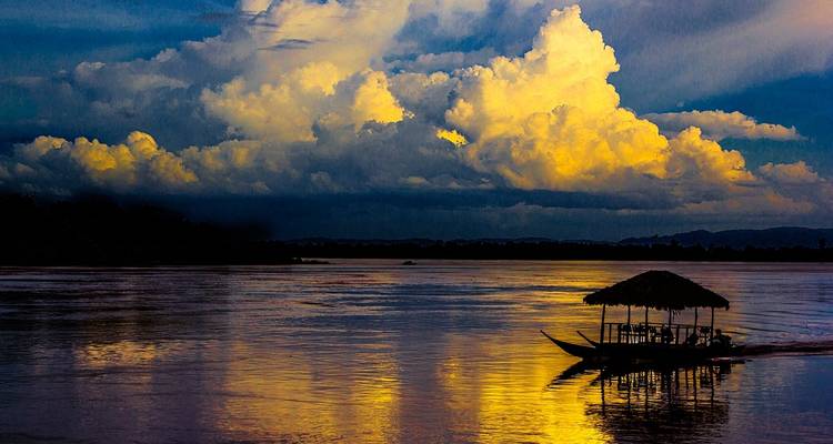 A silhouette of a boat on a river under dramatic clouds at sunset.