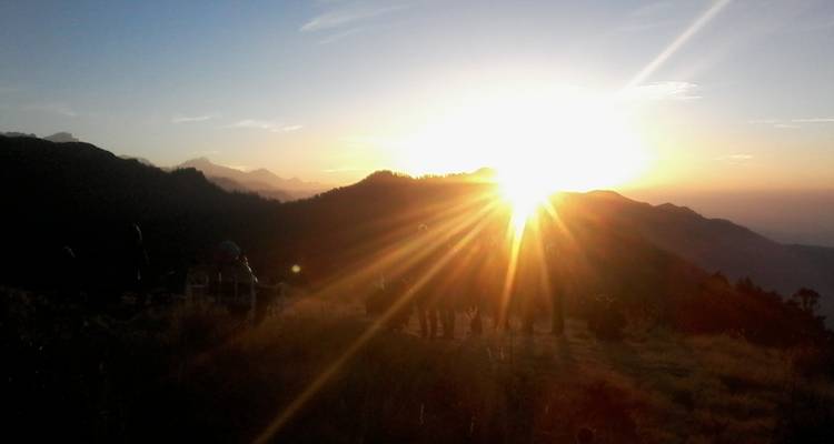Zonsondergangzicht met silhouetten van mensen en bergen.