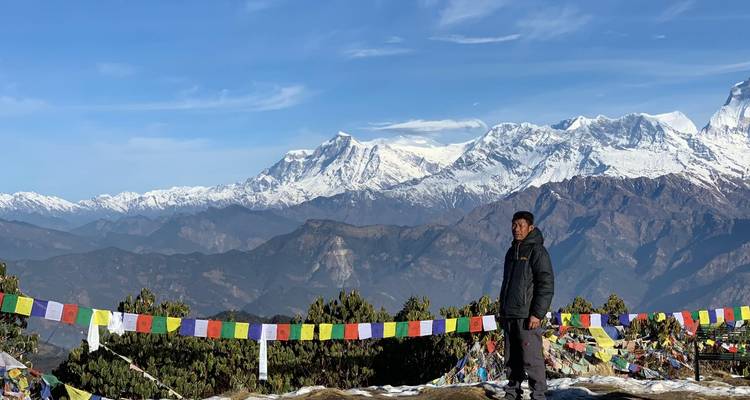 Persoon die staat met gebedsvlaggen en een besneeuwde bergtop op de achtergrond.