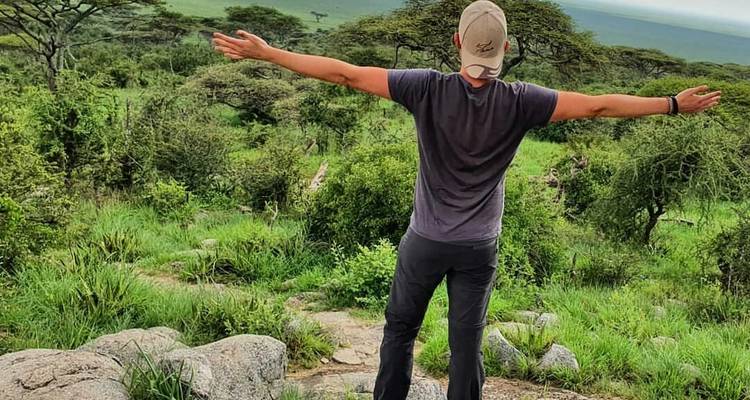 Een persoon met uitgestrekte armen in een weelderig groen landschap.