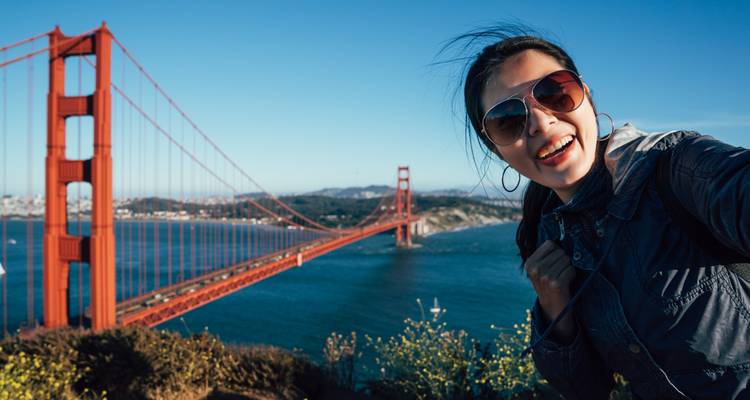 Mujer sonriente tomándose una selfie con el Puente Golden Gate de fondo.