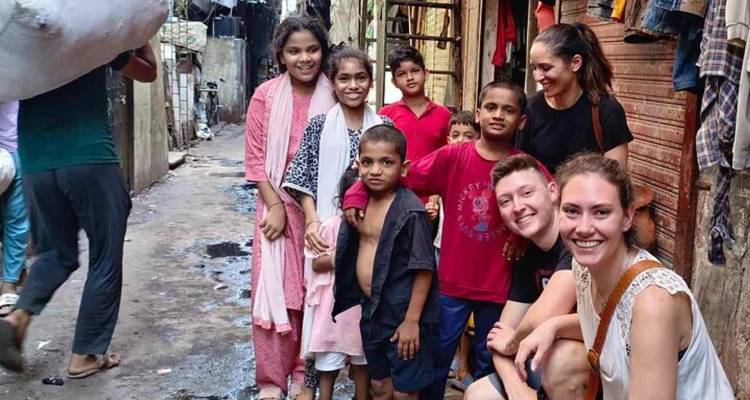Viajeros sonriendo con niños locales en un callejón urbano estrecho.