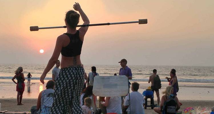 La gente se reúne en una playa al atardecer mientras un artista equilibra un bastón sobre su cabeza.