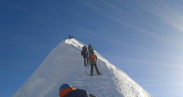 Klimmers in een rij die een steile besneeuwde piek beklimmen.