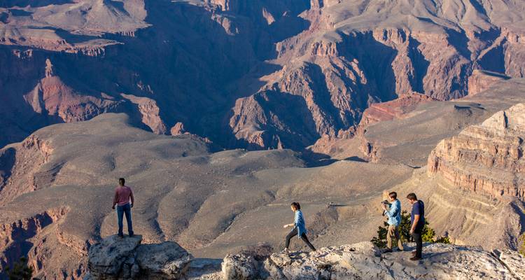 Vrienden lopen langs de rand van een spectaculair Grand Canyon-uitkijkpunt, met één persoon die apart op een rots staat.