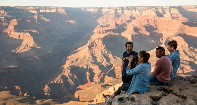 Kleine groep ontspant op een rotsachtige richel met uitzicht op de enorme uitgestrektheid van de Grand Canyon.