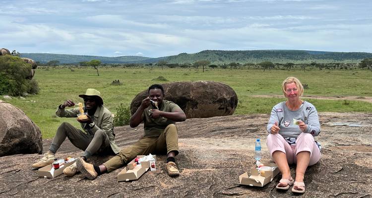 Des gens assis en train de manger en plein air dans un paysage de savane.