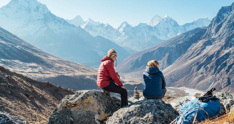 Deux personnes se reposant sur des rochers avec un magnifique panorama montagneux en arrière-plan.