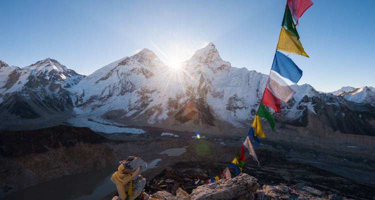 Sommets himalayens avec drapeaux de prière colorés au lever du soleil.