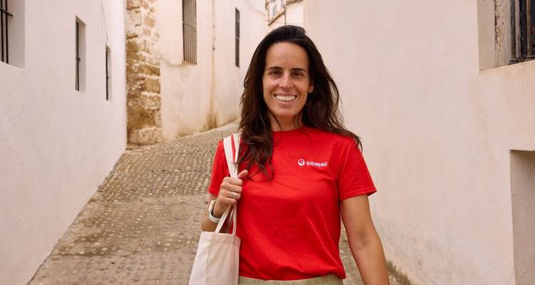 Jeune femme tenant un sac cabas souriant dans une rue étroite blanchie à la chaux en Andalousie