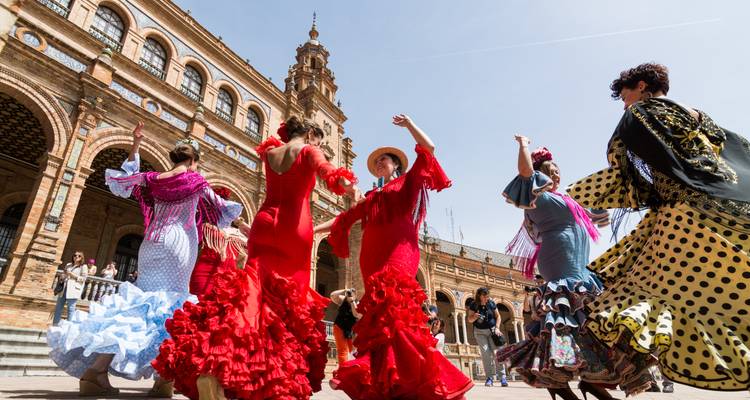 Flamenco-Tänzer in leuchtenden Kleidern wirbeln energisch auf der Plaza de España unter dem strahlenden Himmel von Sevilla.