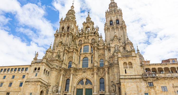 La façade ornée de la Cathédrale de Santiago de Compostela se dresse contre un ciel partiellement nuageux