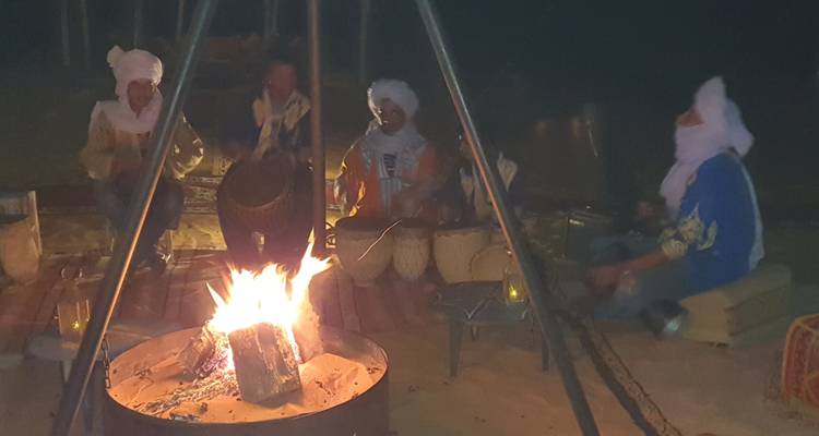 Un groupe de personnes en tenue traditionnelle assises autour d'un feu de joie dans la nuit.