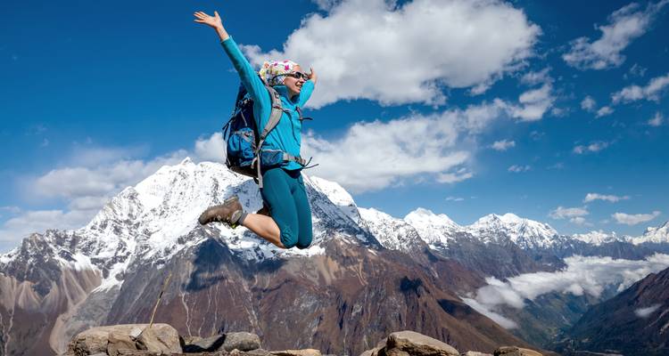 Fröhlicher Wanderer springt vor einer Kulisse schneebedeckter Berge.