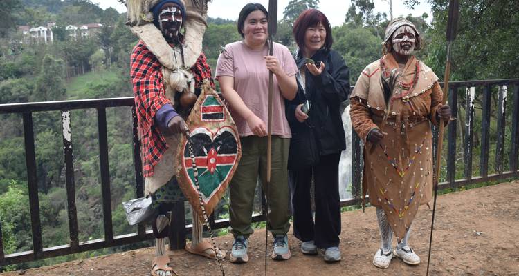 Tourists posing with locals in traditional costumes in front of a forested area.