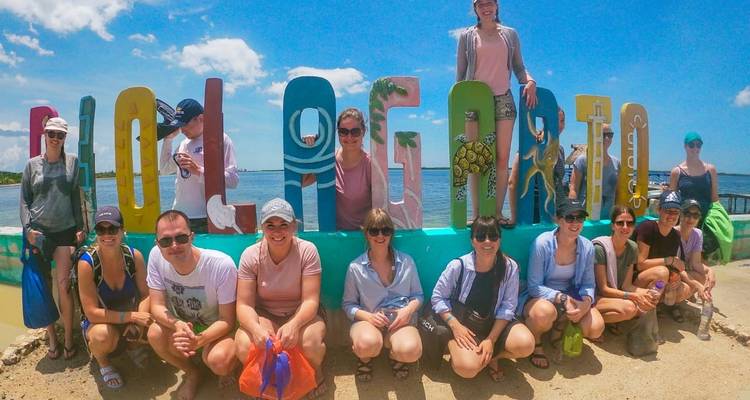 Group photo in front of a colorful sign at a waterside location.