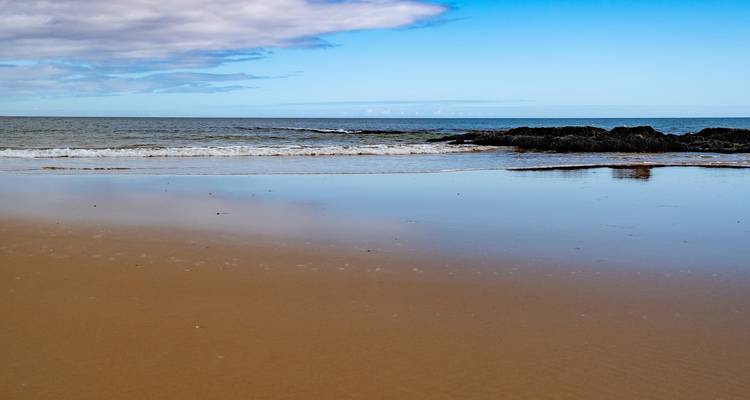 Plage de sable avec des vagues douces et un horizon lointain.