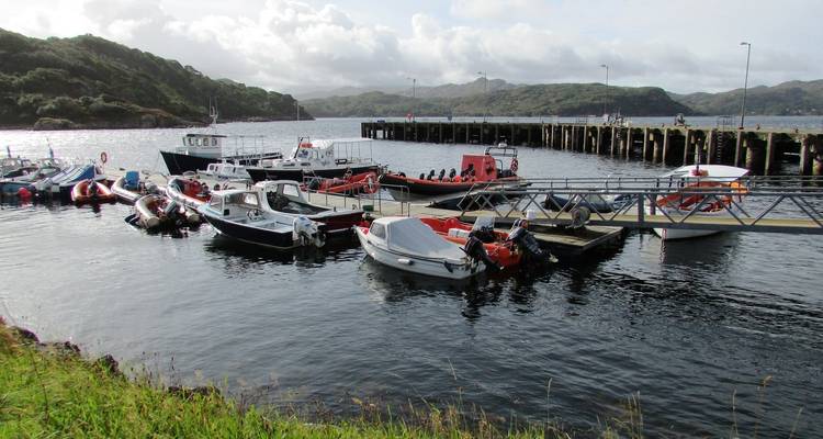 Petits bateaux amarrés à un quai, entourés de collines.