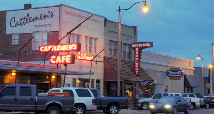 Street view with neon signs and parked cars at dusk.