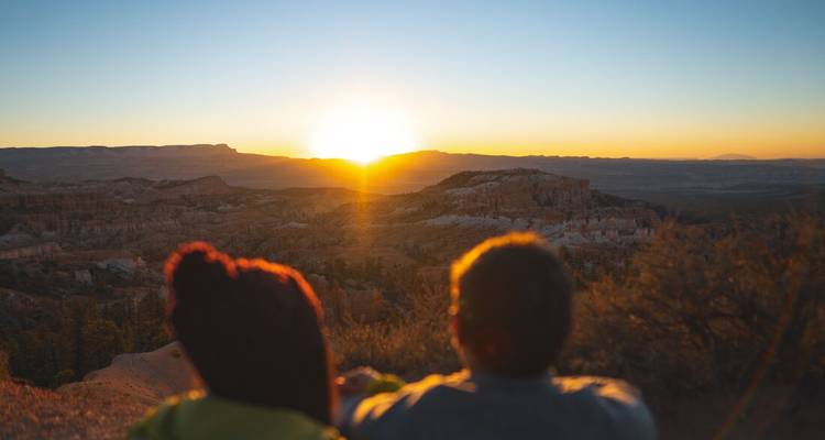 Couple regardant le lever du soleil sur les cheminées de fées orange et le vaste paysage de canyon de Bryce Canyon.