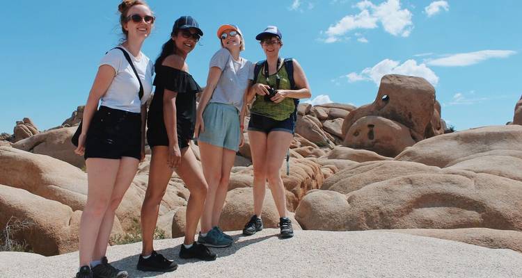 Groupe de quatre femmes posant parmi des rochers de granit lisse et un ciel bleu dans le parc national de Joshua Tree.