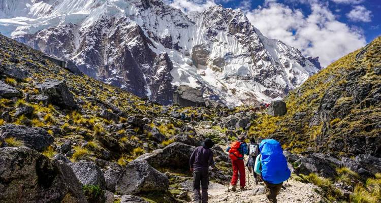 Excursionistas caminando hacia montañas cubiertas de nieve en Perú.